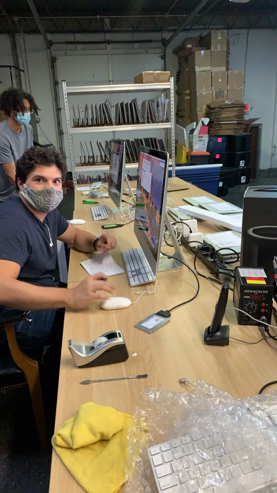 Chris and Chan working at a long workstation with iMacs in the warehouse