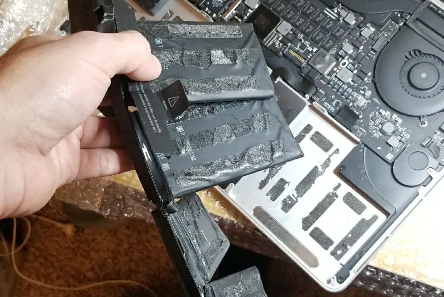 Hand removing a swollen battery from an open MacBook Pro